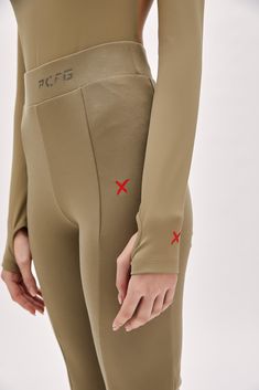 a woman with her hands on her hips wearing tight, beige pants and red crosses