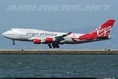 a virgin atlantic airplane taking off from the runway at an airport near the water's edge