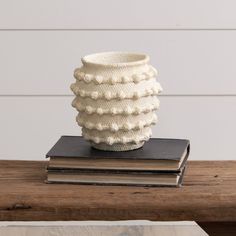 a stack of books sitting on top of a wooden table next to a white vase