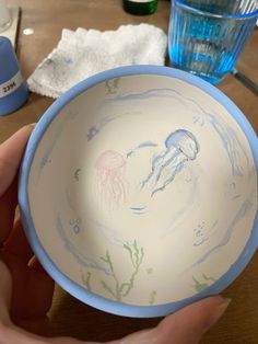 a hand holding a bowl with jellyfish designs on the bottom and blue trim around it