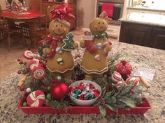 two gingerbread men sitting on top of a red tray filled with candy and candies