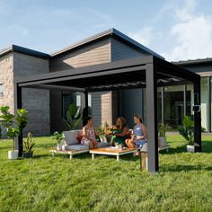 two women sitting on a couch under a pergolan in the grass next to a house