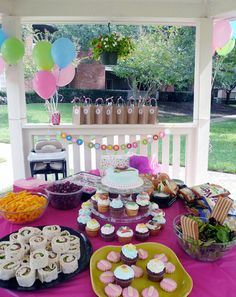 a pink table topped with lots of cupcakes and cake covered in frosting