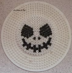 a white plate topped with lots of black beads and a skull on the front side