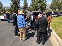 several men in suits and ties are standing near the back of a car with its door open