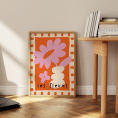 an orange and pink poster on the wall next to a wooden table with a laptop