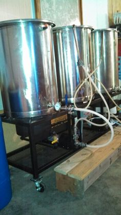 three large stainless steel tanks sitting on top of a wooden pallet next to a blue barrel