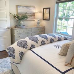 a white bed with blue and white comforter next to a window in a bedroom