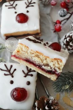 two pieces of cake with white frosting and red cherries on top, sitting next to pine cones