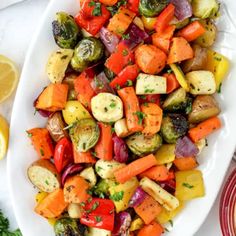 a white plate topped with roasted vegetables next to lemon wedges