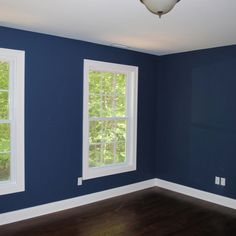 an empty room with blue walls and wood flooring in the foreground, two windows on either side