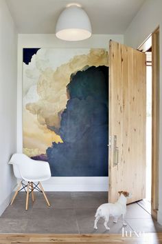 a white chair sitting in front of a painting on the wall next to a wooden door