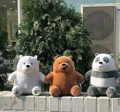 three stuffed animals sitting on top of a brick wall in front of a planter