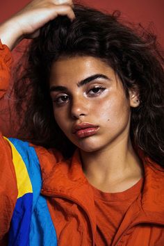 a woman in an orange jumpsuit is holding her hair up and looking at the camera