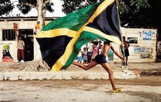 a woman running with a jamaica flag on her back while people watch from the sidelines