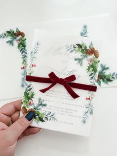 a hand holding a piece of paper with a red ribbon and holly decorations on it