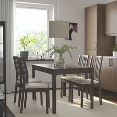 a dining room table with four chairs and a plant in the center, next to a window