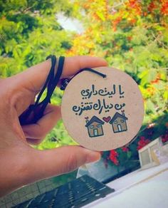 a person holding up a small round ornament with houses on it in front of some trees