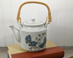 a tea pot sitting on top of a book next to a vase with flowers painted on it