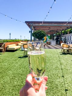 a person holding up a wine glass in front of an outdoor seating area with string lights