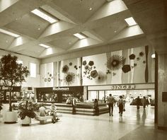 people are walking around in the lobby of a shopping mall, with large windows above them