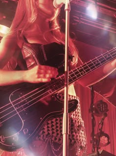 a woman with long blonde hair is playing the bass guitar in front of a microphone