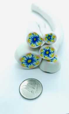 four white and blue flowered beads sitting next to a quarter penny on a white surface