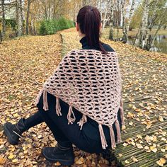 a woman sitting on top of a wooden bench covered in leaves and wearing a crocheted shawl