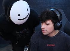 a young man wearing headphones next to a giant stuffed animal with a smile on it's face