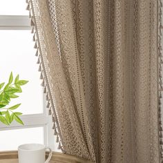 a coffee cup sitting on top of a wooden table next to a window covered in lace