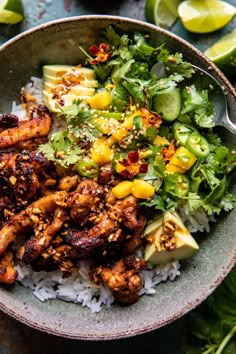 a bowl filled with rice and chicken next to sliced limes, avocado and cilantro