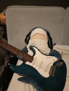 a stuffed animal wearing headphones and holding an electric guitar in its mouth, sitting on a bed