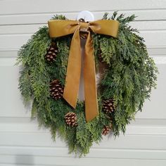 a wreath with pine cones and a bow hanging on a garage door in front of a house