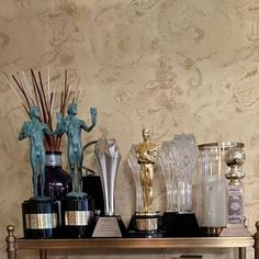 there are many trophies and statues on the shelf in front of the wall papered room