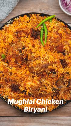 an overhead view of murghai chicken biriyani in a black plate on a wooden table