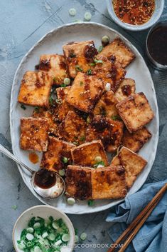 tofu on a white plate with chopsticks next to it and dipping sauce