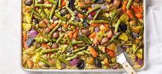 a casserole dish filled with vegetables on top of a white table cloth next to a knife