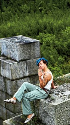 a man sitting on top of a stone wall talking on a cell phone while holding his hand up to his face