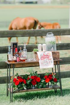 a table with flowers and bottles on it in front of a wooden fence near a horse