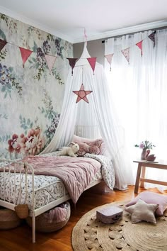 a bedroom with floral wallpaper and pink bedding in front of a white curtained window