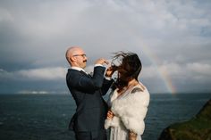 a man and woman standing next to each other in front of the ocean under a cloudy sky