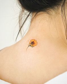 a small sunflower tattoo on the back of a woman's upper back neck