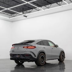 the rear end of a grey mercedes suv in a white room with black and orange rims