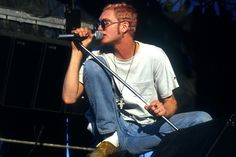 a man sitting on top of a stage with a microphone in his hand and wearing glasses