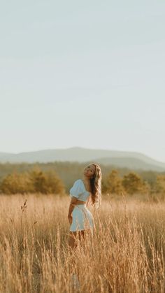 a woman standing in the middle of a field with her arms behind her back, looking into the distance