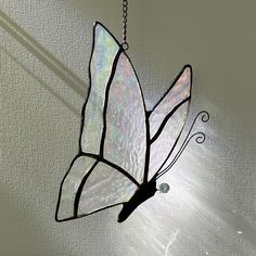 a stained glass butterfly hanging from a chain on a window sill with sunlight streaming through it