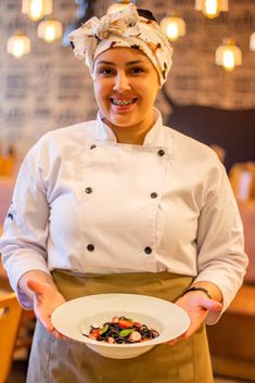 a woman in an apron holding a plate with some food on it and smiling at the camera