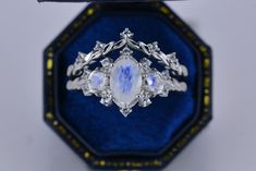 a ring with an oval shaped stone surrounded by smaller round stones in a blue velvet box