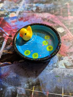 a yellow rubber ducky floating in a blue bowl on top of a colorful surface