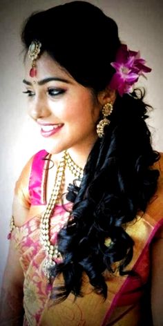 a woman with long black hair wearing a pink and gold saree, smiling at the camera